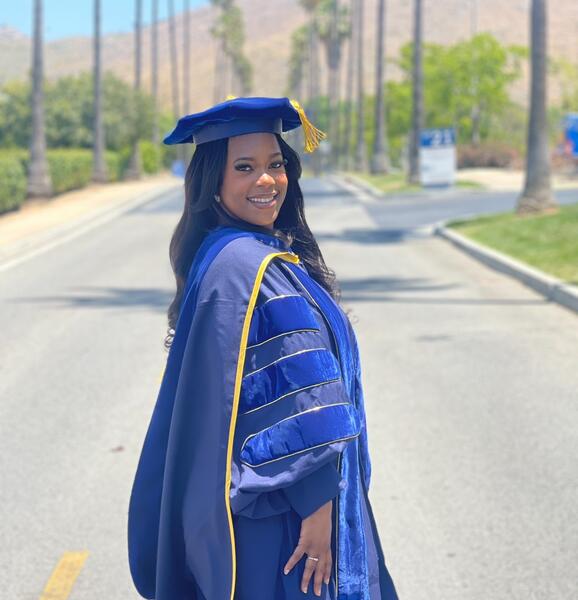 Keziyah Yisrael in graduation regalia on a tree-lined street