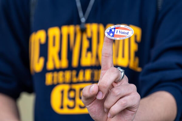 a person wearing a ucr shirt with an I voted sticker on their finger.