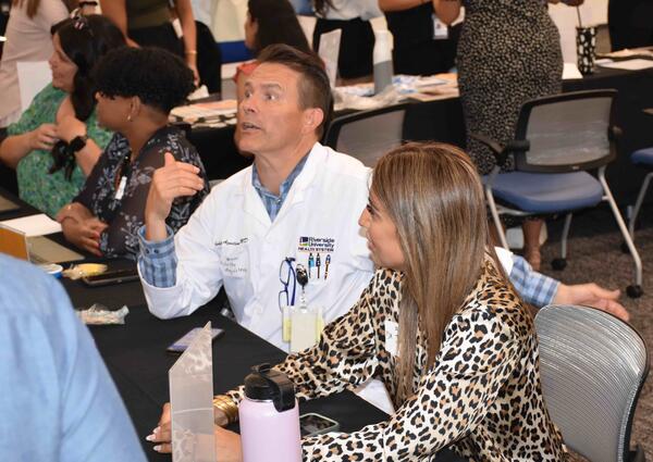 Dr. Aguilera in a white coat sitting at a table at orientation 2024