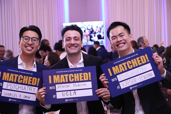 Three medical students hold up signs saying where they will be going for residency.