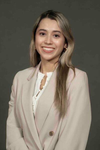 Pamela Munoz wearing a beige jacket against a dark gray background