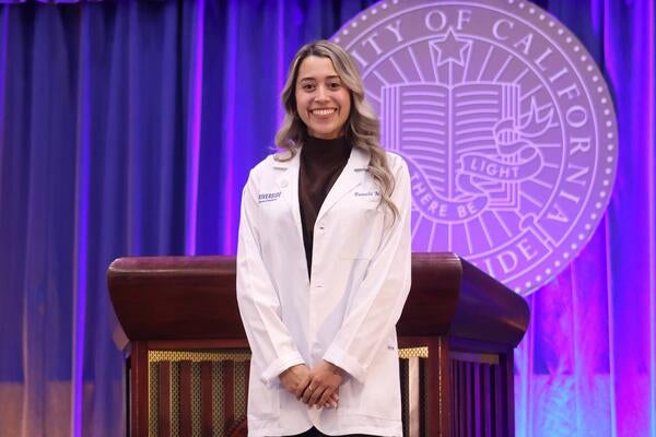 Pamela Munoz wearing her white coat in front of the UCR seal