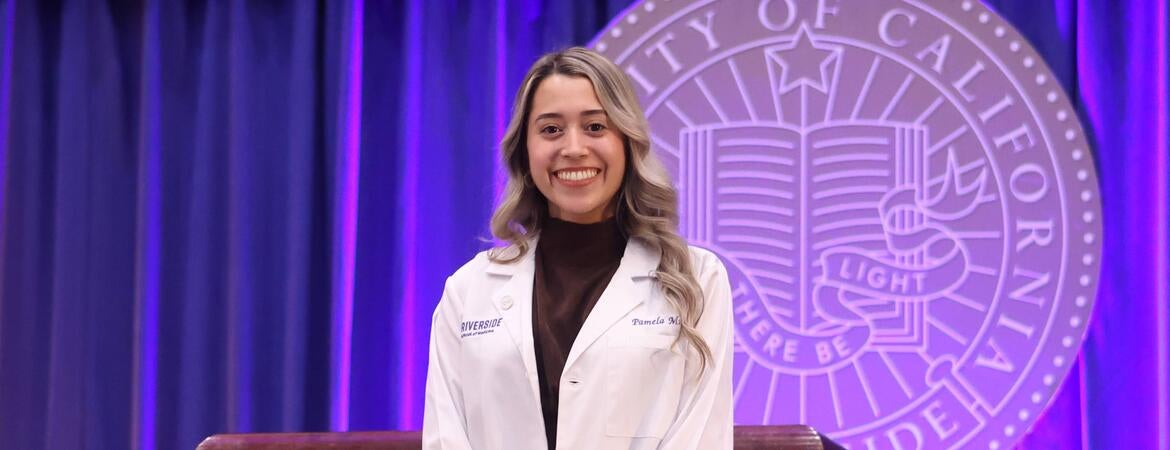 Pamela Munoz wearing her white coat in front of the UCR seal