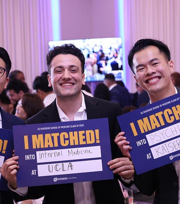Three medical students hold up signs saying where they will be going for residency.