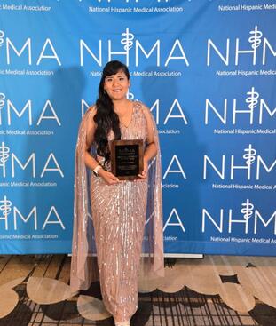 Joslyn Santana in a pink dress holding her NHMA award