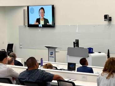Summit attendees sit at tables listening to a speaker on Zoom